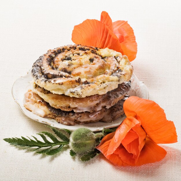 Poppy seed rolls, traditional german Mohnschnecke pastry, on plate with fresh poppy flowers