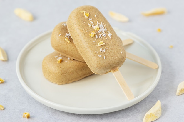 Popsicle with chocolate cashews mango pieces and coconut on a plate