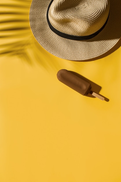 Popside ice cream and hat on bright yellow background with tropical leaf shadow, creative pastel, copy space