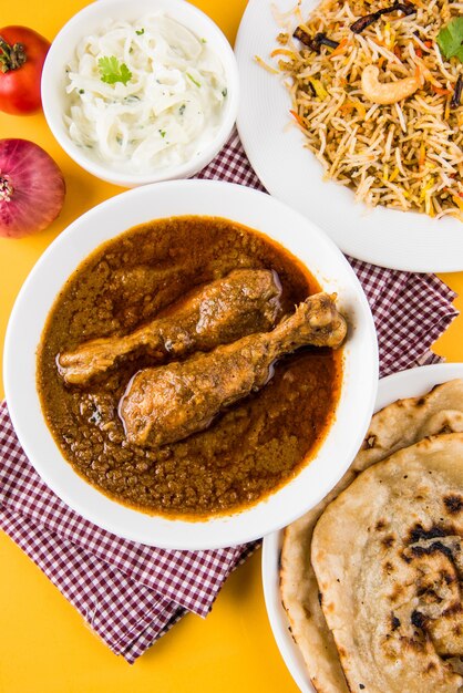 Populaire roodachtige Chicken Curry of Masala, met prominent stuk poot, geserveerd in een kom met Pilau Rice, Chapati of Roti en salade