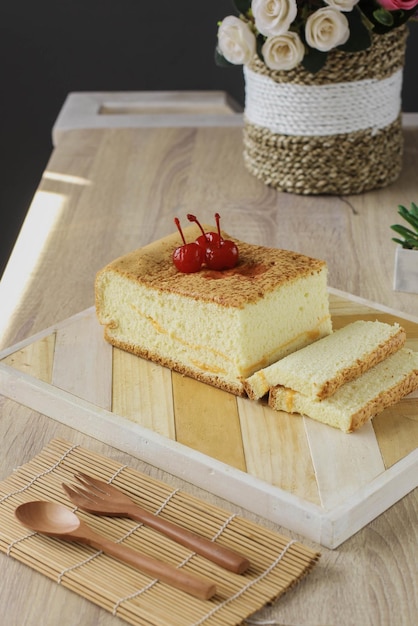 인기 있는 일본 디저트 또는 카스텔라 위에 체리를 얹은 스폰지 케이크가 나무 테이블에 제공됩니다.