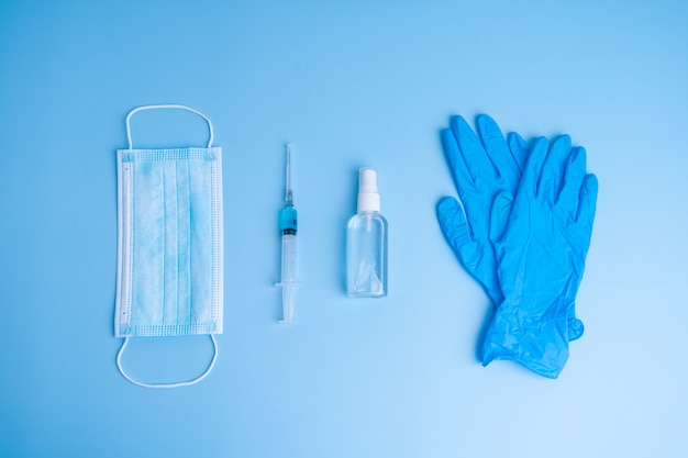 Popular medical antiviral mask, a syringe with a virus vaccine and medical gloves on blue