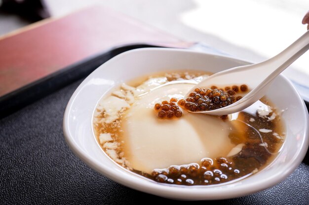 Photo popular taiwan gourmet dessert of tapioca pearl ball bubble mixed bean curd tofu pudding douhua dou hua in white bowl close up lifestyle