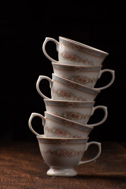 Porcelain cups, beautiful porcelain cups stacked on rustic wood, dark background, selective focus.