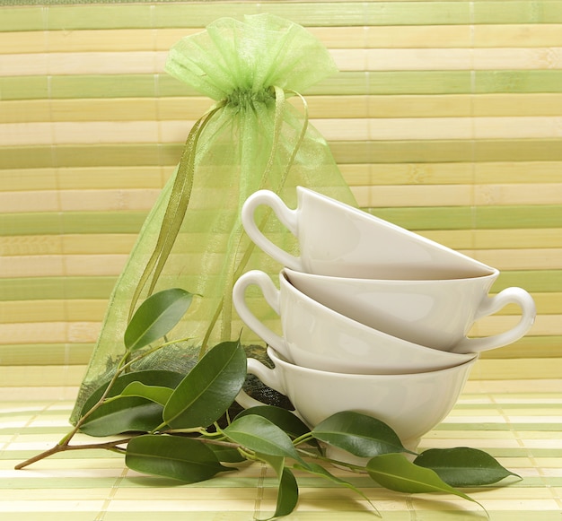 磁器のカップ、緑の葉、縞模様のマットの背景にお茶の袋
