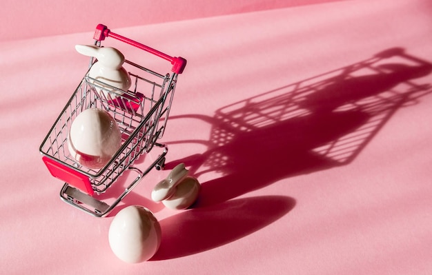 ピンクの背景のポーセランのイースターエッグウサギとショッピングカート