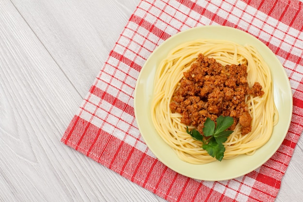 Porcelain plate with spaghetti and bolognese sauce on a kitchen napkin. Top view.