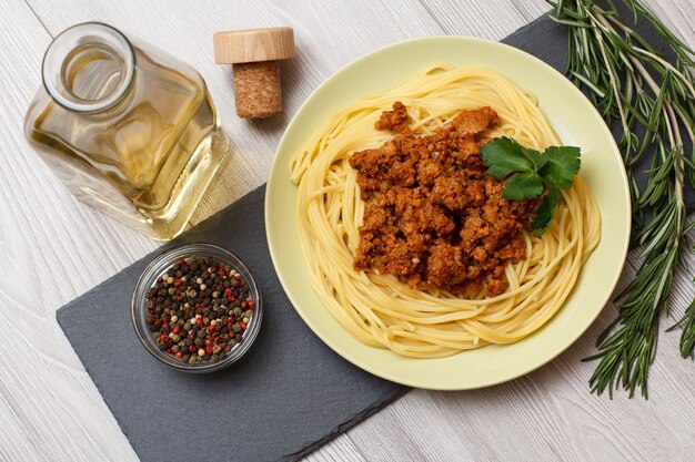 Porcelain plate with spaghetti and bolognese souce, bottle of white wine and allspice peppers. Top view.