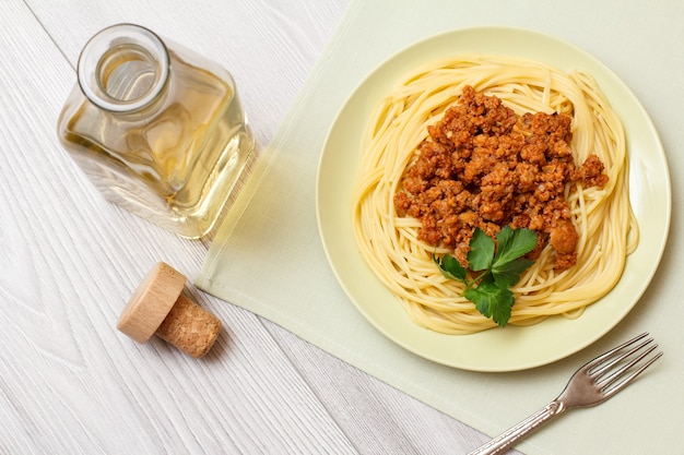 Foto piatto in porcellana con spaghetti e ragù alla bolognese, forchetta in metallo e bottiglia di vino bianco su tavole di legno grigie. vista dall'alto.