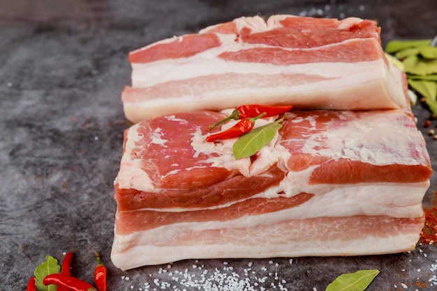 Pork belly meat pieces with hot pepper on a grey background