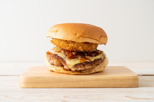 pork burger with cheese, bacon and onion rings on wood board