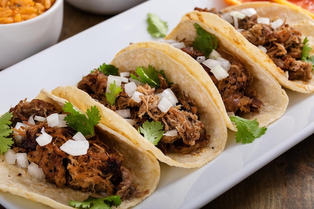 Pork carnitas tacos on corn tortillas with rice and beans