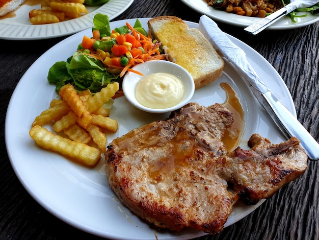 Bistecca di braciola di maiale con patatine fritte e insalata mista su un piatto bianco