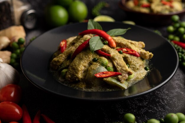 Pork green curry in black plate with spices on black cement background