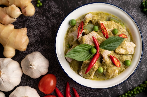 Pork green curry in a white bowl with spices on a black cement background