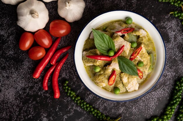 Pork green curry in a white bowl with spices on a black cement background