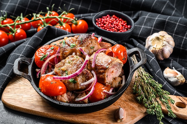 Pork kebab with tomato and pepper in a pan. Meat BBQ.  Black background. Top view