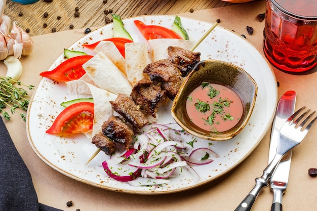 Pork kebabs on a plate with sauce on a wooden table