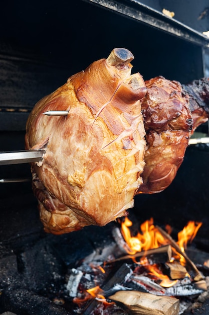 Pork leg are roasted on a spit on a grill outside