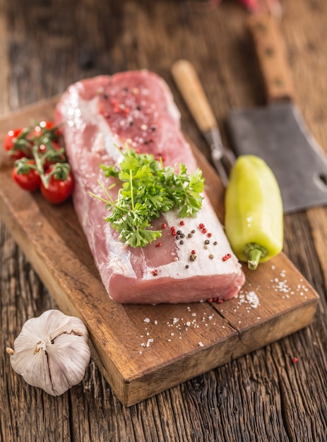 Pork loin fillet parsley herb tomatoes pepper garlic salt and spices on wooden kitchen board.