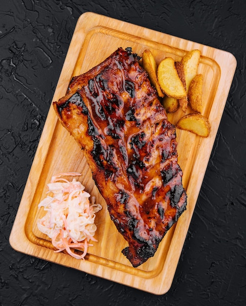 Pork loin ribs served on chopping board and potato wedges