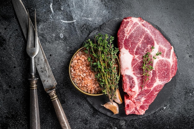 Photo pork loin steak raw neck meat with thyme and salt black background top view