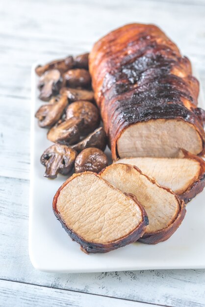 Pork loin wrapped in bacon with roasted mushrooms