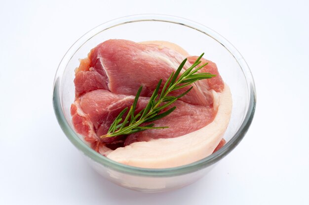 Pork meat in glass bowl with rosemary on white background.