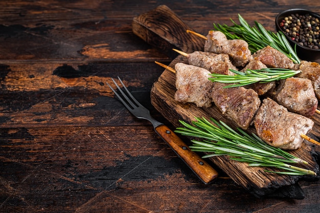 Pork meat Shish kebab on skewers with herbs  on a wooden board. Dark wooden table. Top view. Copy space.