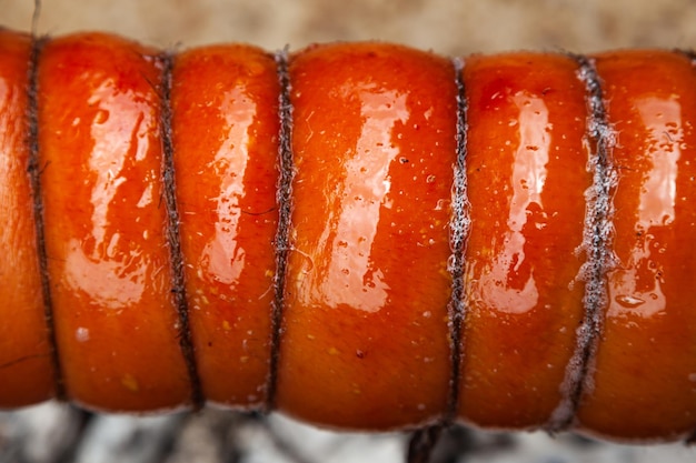 Pork meat with bacon and skin tied with ropes grilled on coals closeup