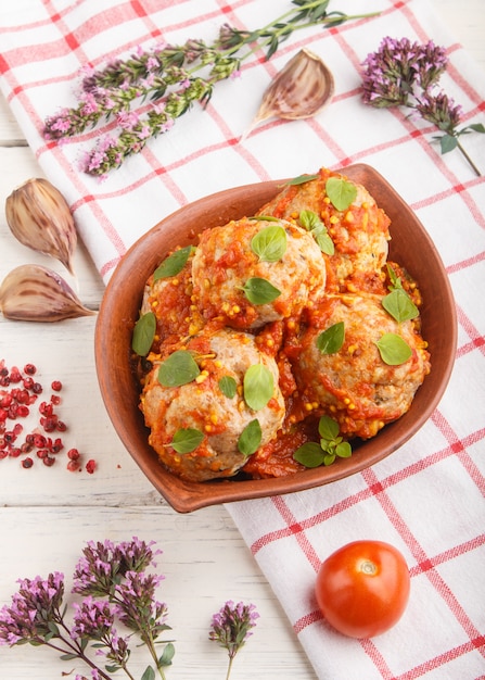 Pork meatballs with tomato sauce, oregano leaves, spices and herbs in clay bowl with linen textile. side view