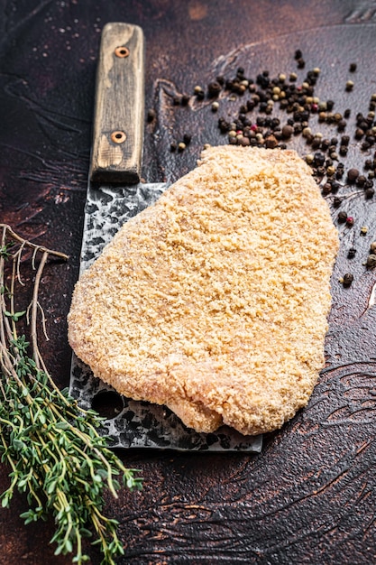 Scaloppa di maiale cruda o cotoletta su una mannaia con erbe aromatiche. sfondo scuro. vista dall'alto.