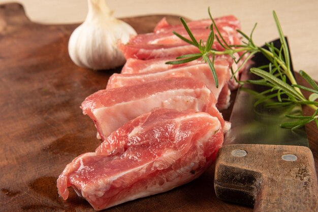 Pork rib, raw pork rib, in pieces and seasoned, with garlic, onion and rosemary on rustic wood and a knife, selective focus.