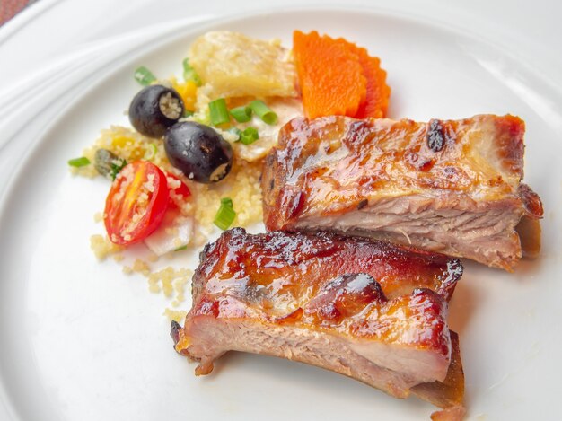 Pork ribs grilled with BBQ sauce and caramelized in honey served with a side dish on a white plate