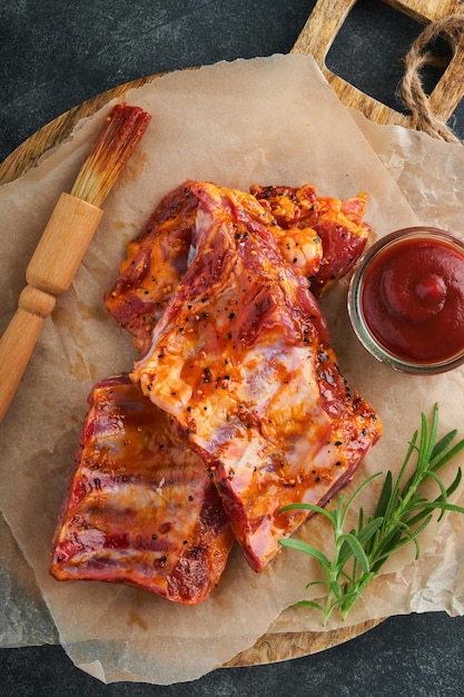 Pork ribs raw meat raw pork ribs in marinade with spices\
rosemary tomato sauce and garlic on old wooden stand on black stone\
table background barbecue concept top view mock up