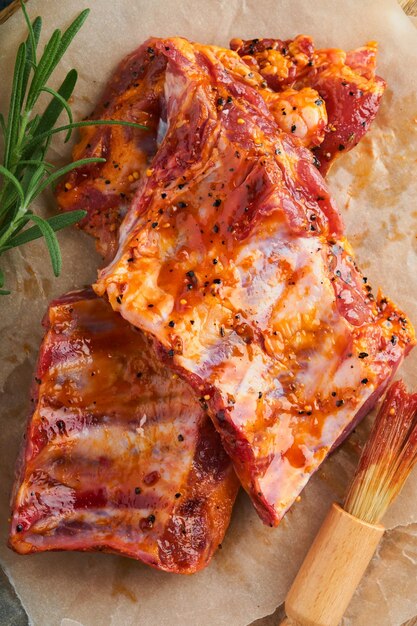 Pork ribs Raw meat Raw pork ribs in marinade with spices rosemary tomato sauce and garlic on old wooden stand on black stone table background Barbecue concept Top view Mock up