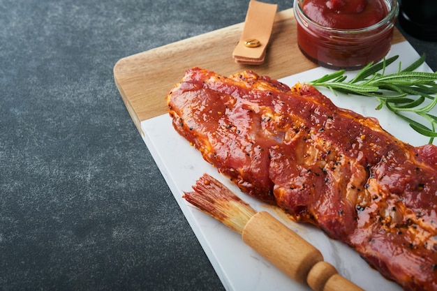 Pork ribs raw meat raw pork ribs in marinade with spices\
rosemary tomato sauce and garlic on white marble stand on black\
stone table background barbecue concept selective focus mock\
up