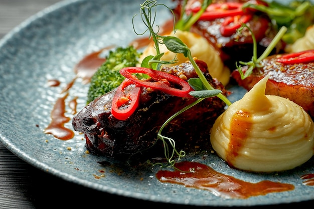 Pork ribs in sweet and sour sauce with vegetable puree and broccoli in a blue plate. BBQ ribs. Selective focus