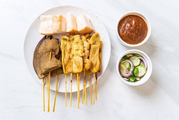 Maiale satay con salsa di arachidi e sottaceti che sono fette di cetriolo e cipolle in aceto