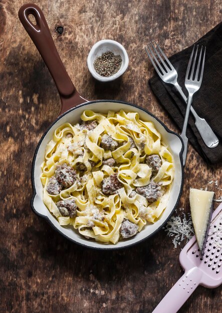 Photo pork sausage and cream sauce fettuccine pasta in a frying pan on a wooden background top view