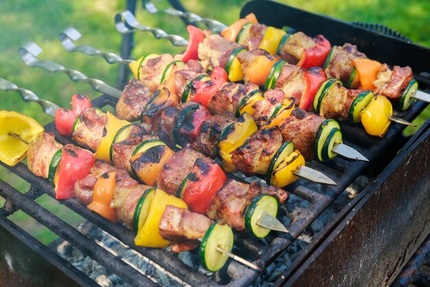 Shish kebab di maiale in fiamme. spiedini di carne fresca appetitosi preparati su una griglia a carbone di legna, all'aperto
