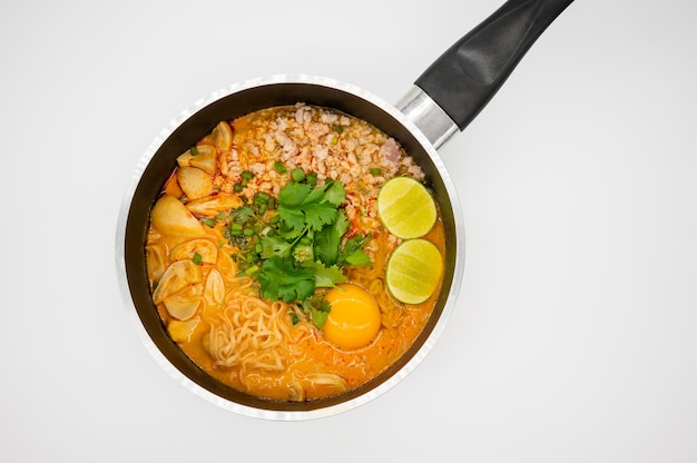 Carne di maiale piccante 'tom yum' con zuppa di noodle istantanei in pentola calda isolata sulla superficie bianca. alimento famoso tailandese.