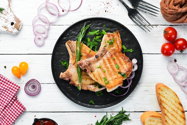 검은 접시에 로즈마리와 채소를 넣은 뼈에 있는 돼지고기 스테이크 상위 뷰 무료 복사 공간