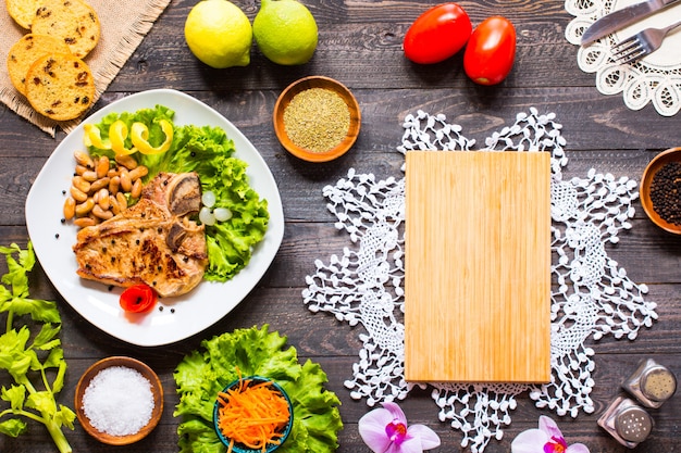 Pork steak homemade cooking with spices leaves lettuce on wooden cutting board, and a dish,