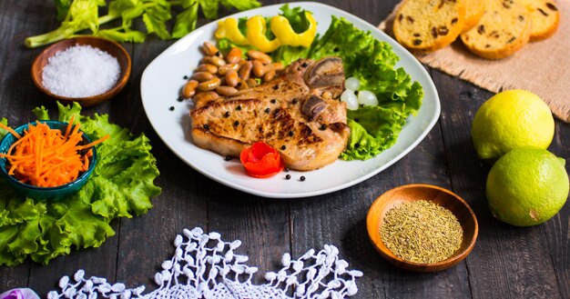 Pork steak homemade cooking with spices leaves lettuce on wooden cutting board, and a dish,