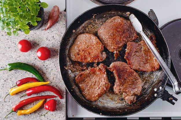 Pork steak roast on rustic pan, fresh hot chili peppers, tomato and herbs.