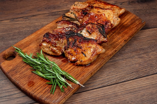 Pork steak and sprig of rosemary on wooden cutting board.