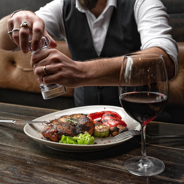 Pork steak with grilled vegetables is peppered by a man having lunch in a restaurant