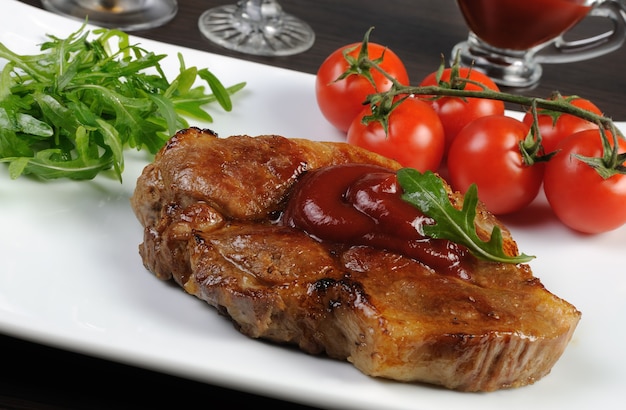 Foto bistecca di maiale con ketchup, rucola, pomodorini