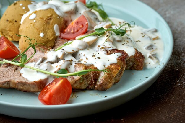 Pork steak with mushroom cream sauce and potatoes in a blue plate on a brown background